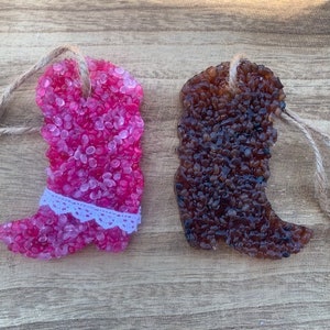 May include: Two decorative cowboy boot air fresheners. One is pink with a white lace trim, the other is brown. Both are made of small, round beads and have a twine loop for hanging. The boots are displayed on a wooden surface.