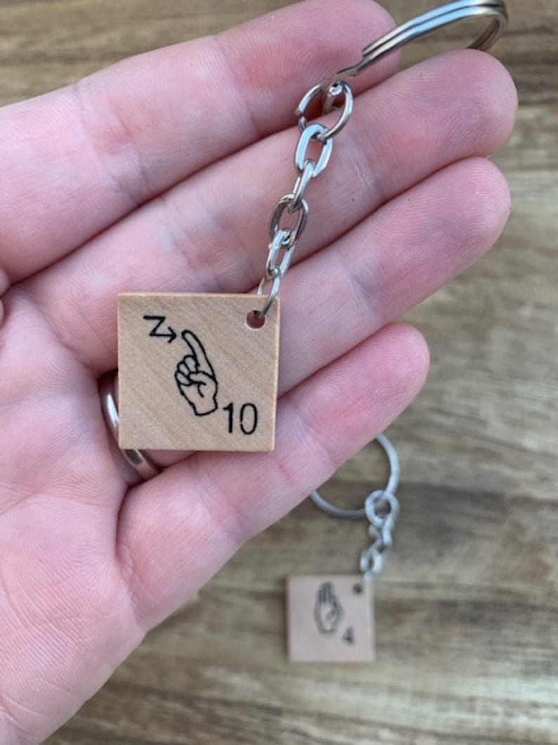 May include: A wooden keychain with two square tags. The tags feature a hand sign for the number 10 and the number 4. The keychain is attached to a silver chain.