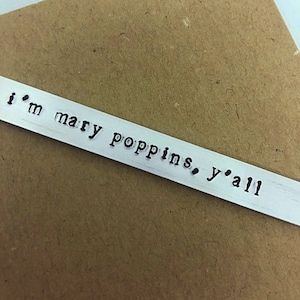 May include: A silver metal bookmark with the text "i'm mary poppins, y'all" engraved on it.