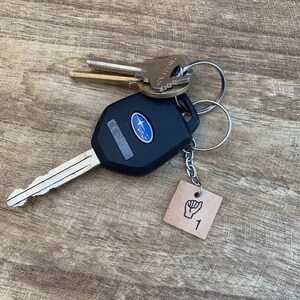 May include: A black car key with a silver key ring and a brown leather keychain with a black hand sign and the number 1.