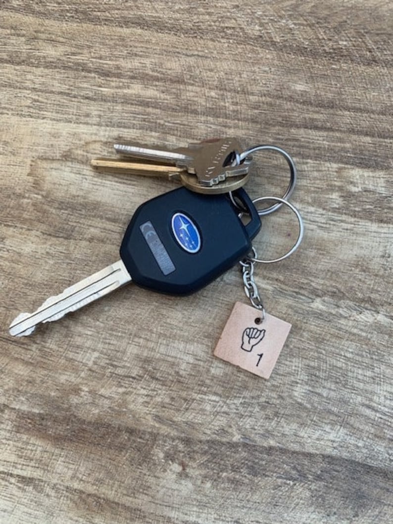 May include: A black car key with a silver key ring and a brown leather keychain with a black hand sign and the number 1.