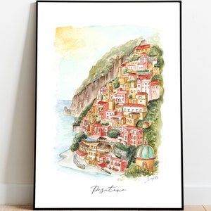 May include: Watercolor painting of Positano, Italy, featuring colorful buildings cascading down a hillside towards the sea. The artwork is framed in black and includes the town's name in cursive script.