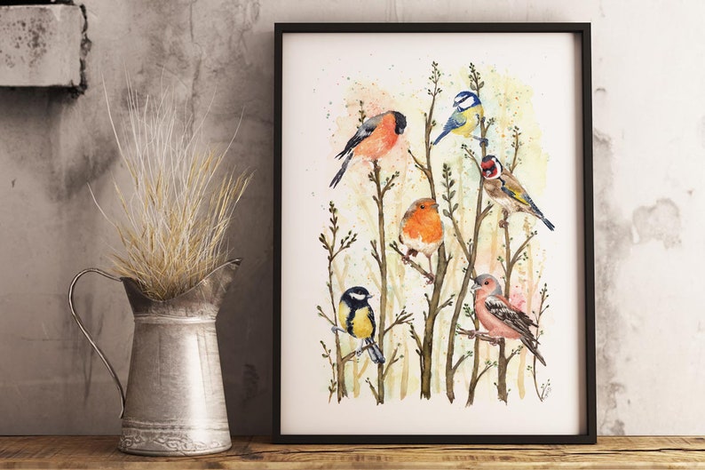 May include: A framed watercolor print featuring several colorful birds perched on tree branches. The birds include a red bullfinch, a blue tit, a robin, and a goldfinch. The artwork has a soft, natural aesthetic, with a neutral background.