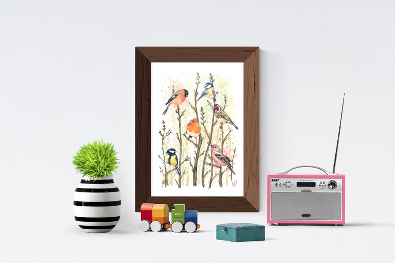 May include: A framed watercolor print featuring several colorful birds perched on branches. The artwork is in a dark brown frame and is displayed on a white wall. A small, decorative green plant in a black and white striped vase, a toy train, and a pink radio are also visible.