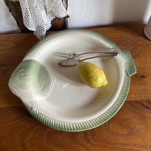 Pode incluir: Um prato de servir de cerâmica branca em forma de peixe com uma borda verde e um limão no topo. O prato está sobre uma superfície de madeira.
