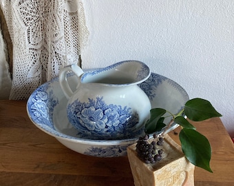 Può includere: Un'anfora e un lavandino in porcellana blu e bianca con motivi floreali. L'anfora è all'interno del lavandino. Un sapone con un rametto di foglie verdi è in primo piano.