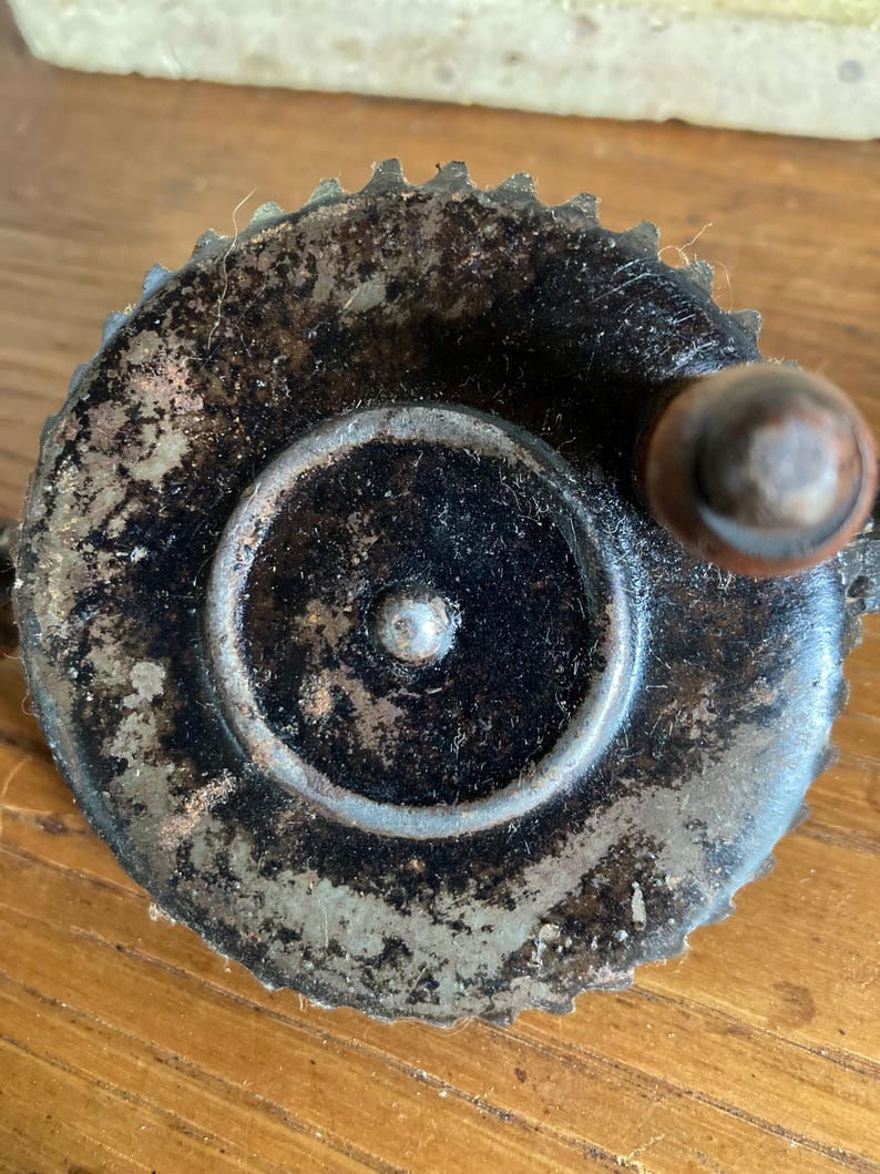 Pu&ograve; includere: Una manovella a mano vintage in metallo con finitura nera e bordo dentato. La manovella ha un piccolo pomello rotondo in metallo sul lato.