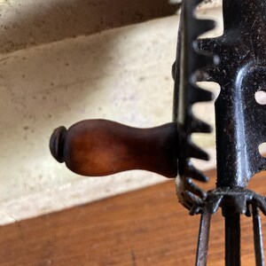 Pu&ograve; includere: Un frullino vintage a manovella con manico in legno e telaio in metallo nero. Il frullino ha quattro lame in metallo e un meccanismo a ingranaggi.