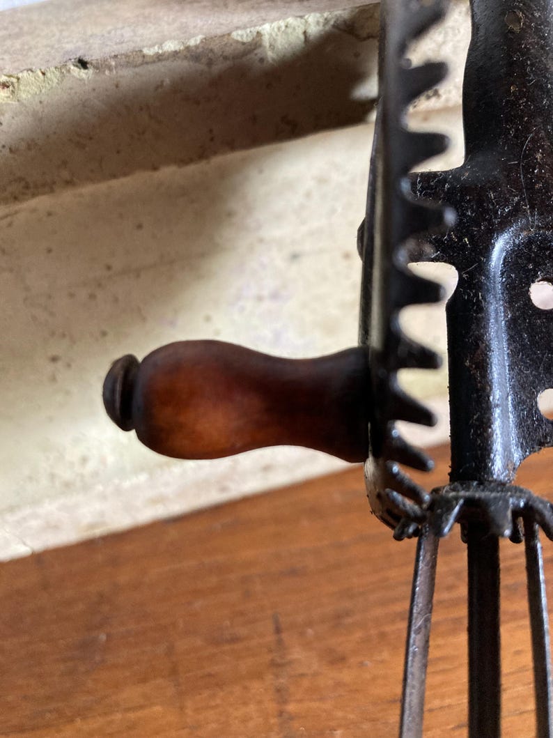 Pu&ograve; includere: Un frullino vintage a manovella con manico in legno e telaio in metallo nero. Il frullino ha quattro lame in metallo e un meccanismo a ingranaggi.