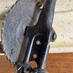 Pu&ograve; includere: Un macinino per alimenti vintage a manovella con corpo in metallo nero e una lama seghettata. Il macinino ha un manico in legno e tre lame in metallo.