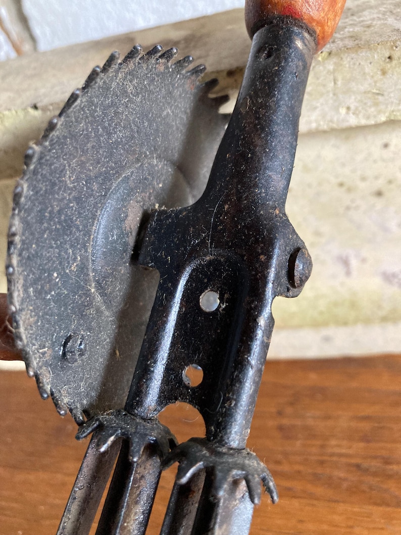 Pu&ograve; includere: Un macinino per alimenti vintage a manovella con corpo in metallo nero e una lama seghettata. Il macinino ha un manico in legno e tre lame in metallo.