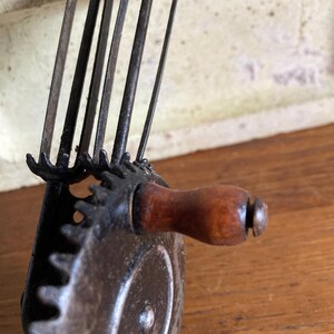 Pu&ograve; includere: Primo piano di uno sbucciatore di mele vintage a manovella, in metallo, con manico in legno. Lo sbucciatore ha un sistema di ingranaggi e pi&ugrave; lame.