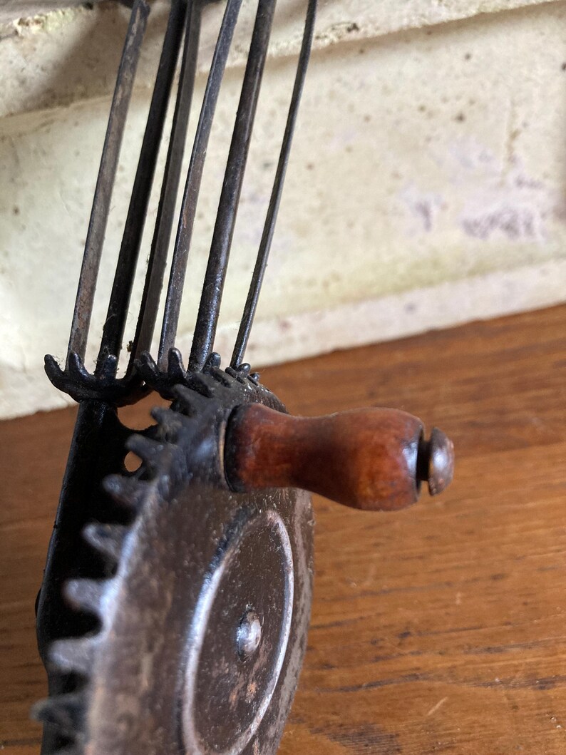 Pu&ograve; includere: Primo piano di uno sbucciatore di mele vintage a manovella, in metallo, con manico in legno. Lo sbucciatore ha un sistema di ingranaggi e pi&ugrave; lame.