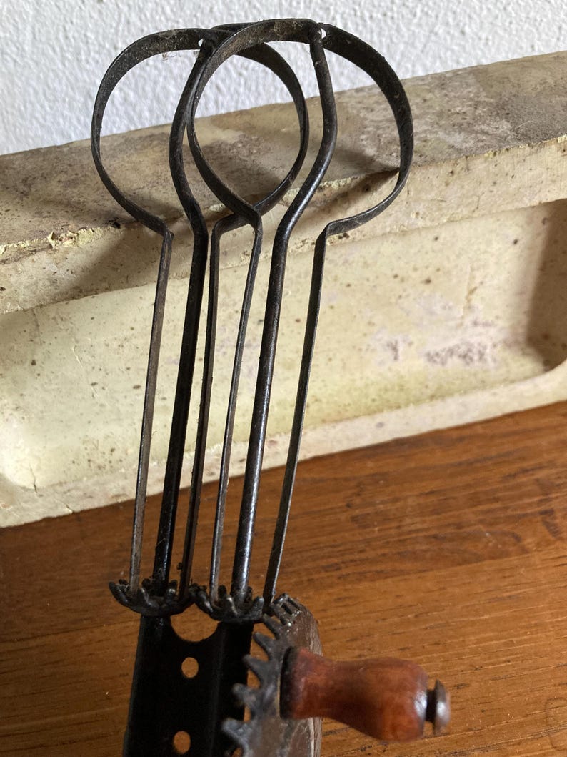 Pu&ograve; includere: Sbattitore per uova antico a manovella con tre fruste in metallo e un manico in legno. Lo sbattitore per uova &egrave; in metallo nero e ha un design a forma di ingranaggio.
