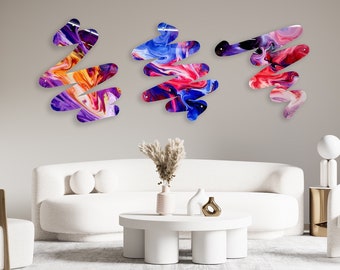 May include: Three abstract wall art pieces in a modern living room. The pieces are made of colourful, swirling acrylic paint on a white background. The pieces are arranged in a row on the wall, with the largest piece in the centre.