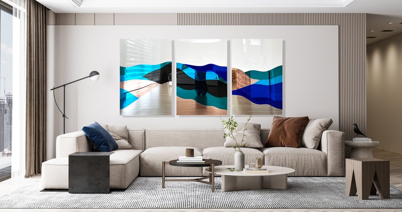 Op de afbeelding: Een modern woonkamerinterieur met een hoekbank, een salontafel en een driedelig abstract kunstwerk in blauwe, turquoise en koperkleurige tinten.