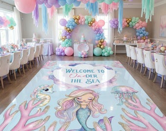 May include: A mermaid-themed party setup with a light blue floor featuring a mermaid, seahorse, and jellyfish illustrations. The floor has the text "Welcome to Under the Sea." Pastel balloons and decorations adorn the room.