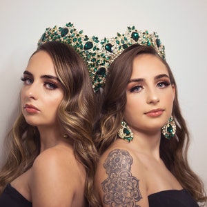 Peut inclure: Deux femmes portant des couronnes et des boucles d'oreilles assorties en or et en pierres précieuses vertes. La femme de droite a un tatouage de mandala noir et gris sur le haut du bras.