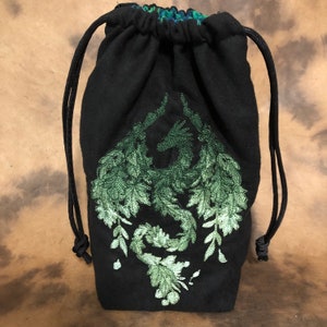 May include: Black drawstring bag with a green embroidered dragon design. The dragon is made of leaves and vines. The bag has a black drawstring closure and a patterned interior.