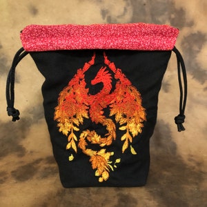 May include: Black drawstring bag with a red and white patterned top. The bag features an embroidered orange and yellow dragon design. Black drawstring cords are visible on the sides.