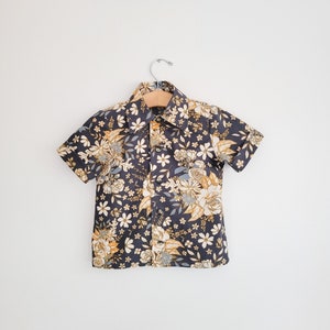 May include: A short-sleeved button-up shirt with a floral print in shades of blue, yellow, and white on a dark blue background.