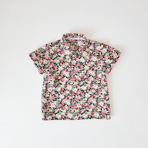 Könnte beinhalten: Ein schwarzes Kurzarmhemd mit einem Blumendruck mit rosa, gelben und weißen Blumen.