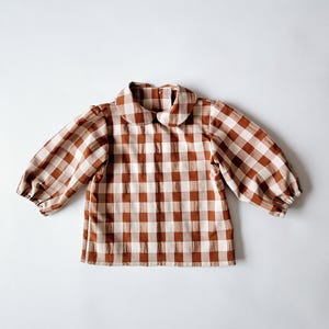 May include: A brown and white gingham button-up shirt with a peter pan collar and long sleeves.