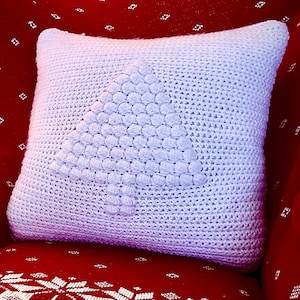 May include: A white crocheted pillow with a raised, textured Christmas tree design sits on a red armchair with a white snowflake pattern. The armchair is in front of a decorated Christmas tree.