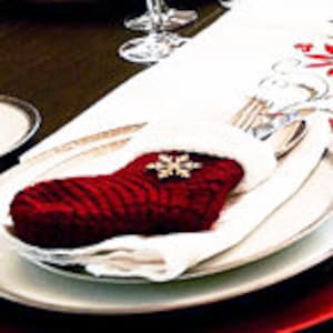 May include: A festive holiday table setting with red and white plates, a white tablecloth with a red floral pattern, and red napkins with a snowflake embellishment.