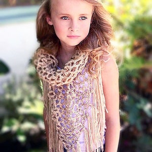 May include: A young girl wearing a light purple sleeveless top and a crocheted beige shawl with fringe. The shawl has a delicate openwork pattern.