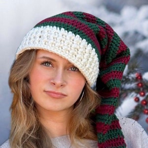 May include: A woman wearing a white and green striped crocheted hat with a long, pointed tail. The hat has a white pompom on the end of the tail.