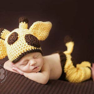 Pode incluir: Um bebê recém-nascido vestindo um traje de girafa de crochê amarelo e marrom. O traje inclui um chapéu com orelhas e uma calça com cauda.