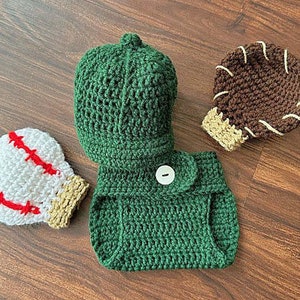 May include: A green crocheted diaper cover with a button closure, a green crocheted baseball cap, a white crocheted baseball, and a brown crocheted baseball mitt.