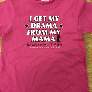 May include: Pink t-shirt with a white graphic that says "I get my drama from my mama and we're both all Cowgirl. Cowgirls Unlimited."
