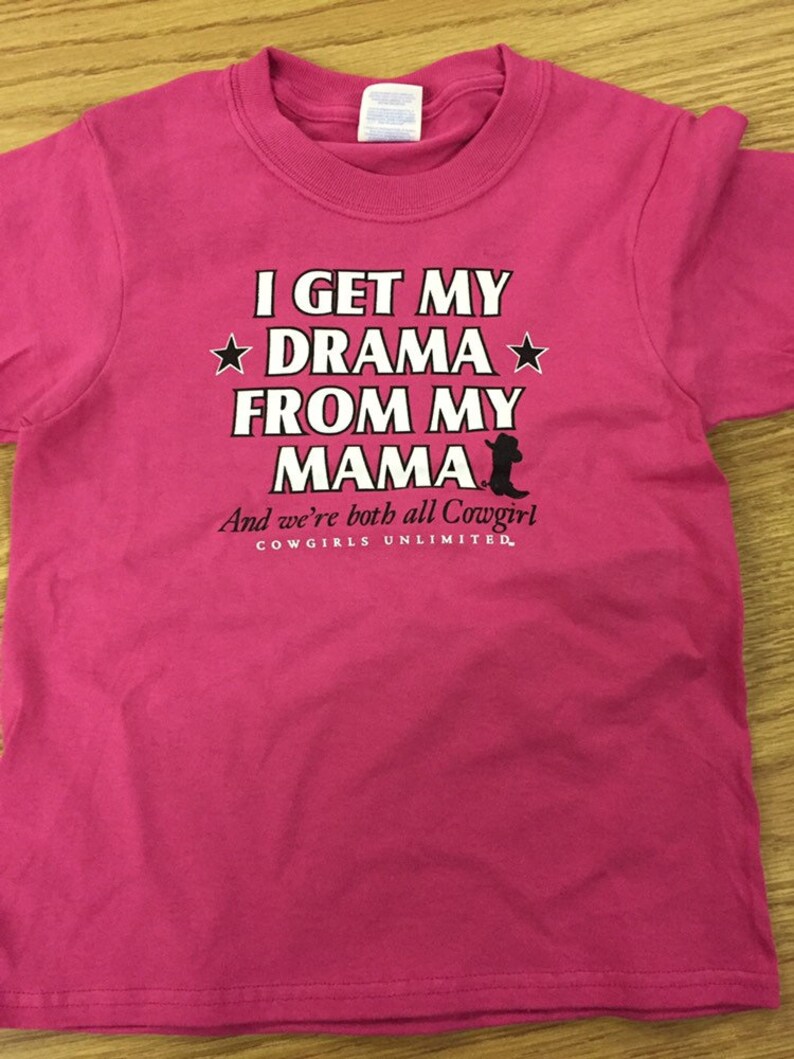 May include: Pink t-shirt with a white graphic that says "I get my drama from my mama and we're both all Cowgirl. Cowgirls Unlimited."