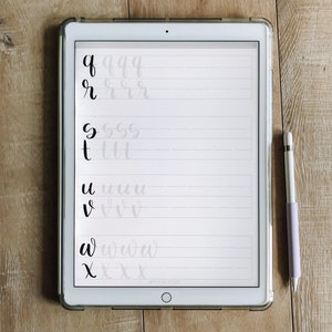 May include: A white iPad with a black screen displaying handwritten letters of the alphabet in cursive. The letters are written in black ink on a white background with gray lines. A purple stylus is lying on a wooden surface next to the iPad.