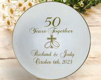 May include: A white decorative plate with gold trim, featuring the text "50 Years Together" and the names "Richard & Judy" with the date "October 6th, 2023". The design includes a cross and wedding rings.