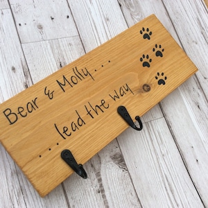 May include: Wooden sign with the text "Bear & Molly... lead the way" and paw prints. The sign has two black metal hooks.