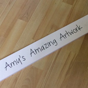 May include: White wooden sign with black marker writing that says "Amy's Amazing Artwork".