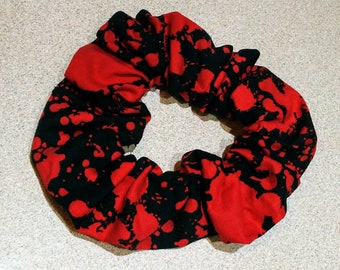 Puede incluir: Scrunchie rojo y negro con un diseño de pintura salpicada.