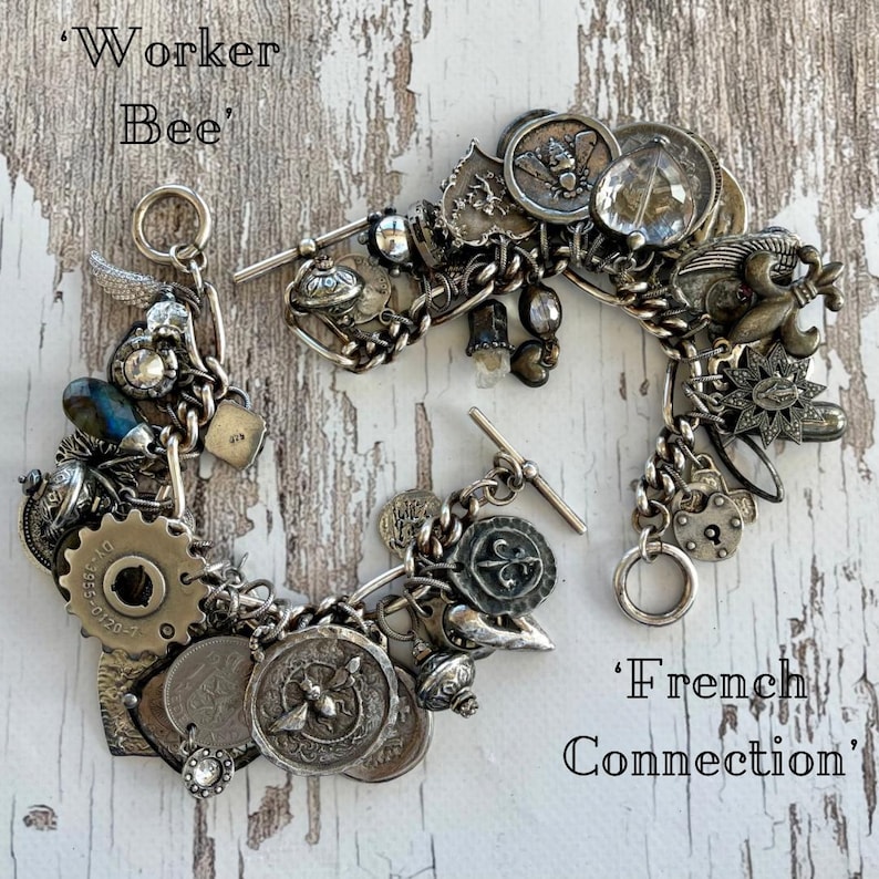Puede incluir: Dos pulseras de plata con dijes de estilo vintage, incluyendo monedas, engranajes y medallones. Una pulsera est&aacute; etiquetada como 'Worker Bee', y la otra como 'French Connection'. Se exhiben sobre una superficie de madera blanca desgastada.