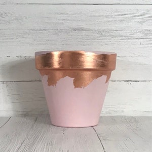 May include: A pink terracotta planter with a copper metallic rim and a copper metallic design on the front.
