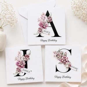 Puede incluir: Tarjetas de felicitaci&oacute;n cuadradas blancas con una letra inicial negra, adornos florales y la frase "Happy Birthday". Cada tarjeta tiene una etiqueta con un nombre: Alice, Janice y Susan. Las tarjetas est&aacute;n decoradas con flores rosas y moradas.