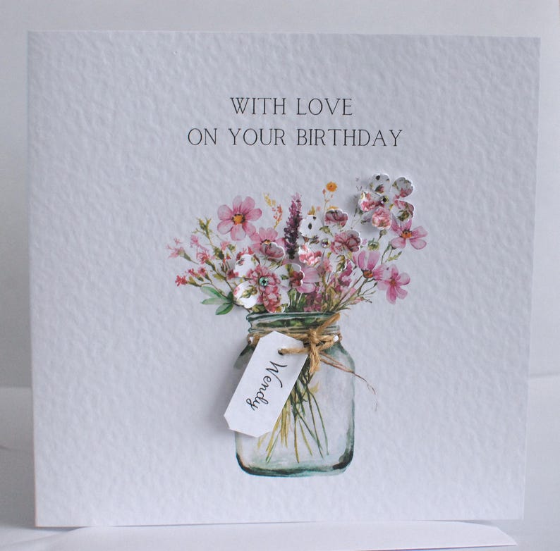 May include: A handmade birthday card with a watercolor illustration of a bouquet of pink and white flowers in a mason jar. The card reads "WITH LOVE ON YOUR BIRTHDAY" and has a tag that says "Wendy".