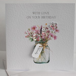 May include: A handmade birthday card with a watercolor illustration of a mason jar filled with pink and white flowers. The card reads "WITH LOVE ON YOUR BIRTHDAY" and has a small tag that says "Wendy".