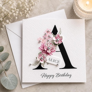 Puede incluir: Tarjeta de felicitaci&oacute;n blanca con una gran letra "A" negra decorada con flores rosas y detalles plateados. La tarjeta dice "ALICE" y "Feliz Cumplea&ntilde;os". Incluye un sobre blanco.