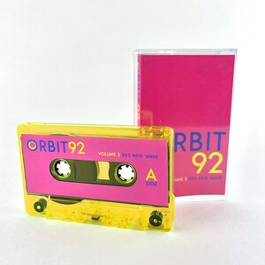 May include: A yellow cassette tape with a pink label. The label says "ORBIT 92 VOLUME 2 80'S NEW WAVE" and "A SIDE".