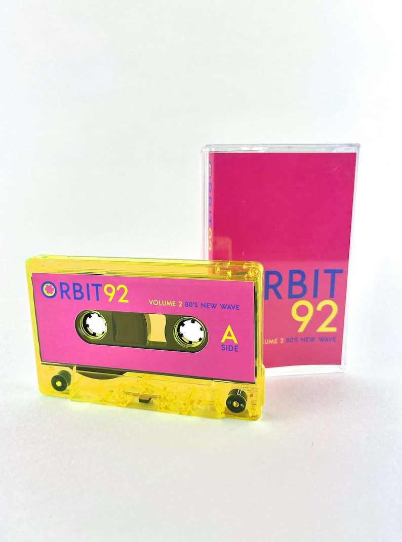 May include: A yellow cassette tape with a pink label. The label says "ORBIT 92 VOLUME 2 80'S NEW WAVE" and "A SIDE".