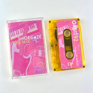 May include: A clear cassette case and a yellow cassette tape sit side-by-side. The cassette case has a pink and white design with the words "Shoegaze 90's Mix". The yellow cassette tape has the words "Orbit 92" and "Volume 1 90's Shoegaze".