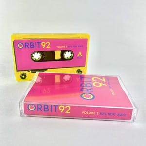 May include: A yellow cassette tape with a pink label. The label says "ORBIT92 VOLUME 2 80'S NEW WAVE".